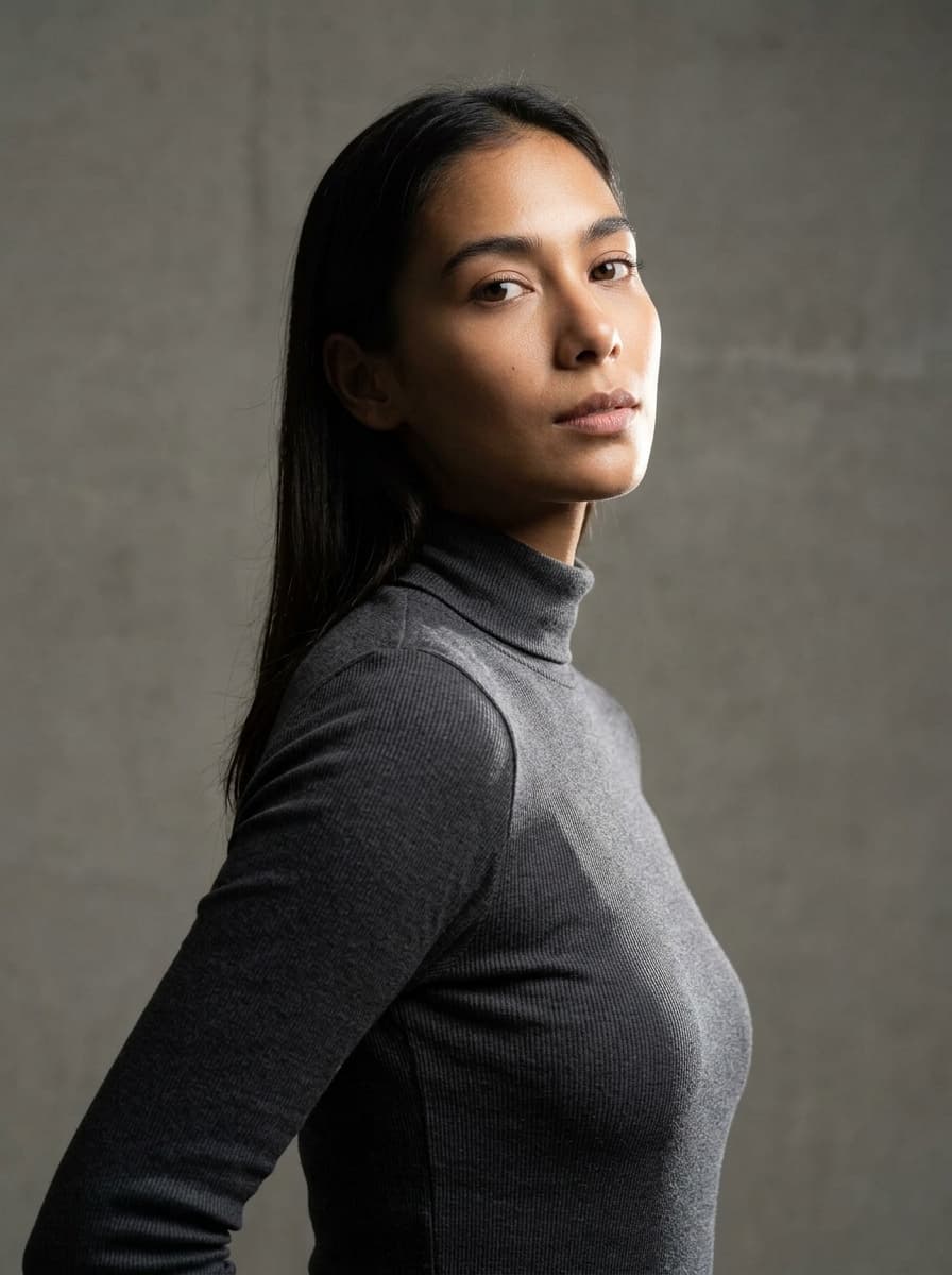 Editorial fashion portrait of a model in a charcoal turtleneck against a textured gray background